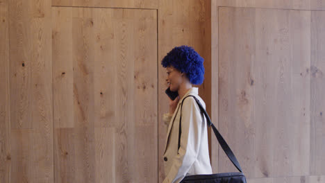 Happy-biracial-businesswoman-with-blue-afro-talking-on-smartphone-in-office,-slow-motion