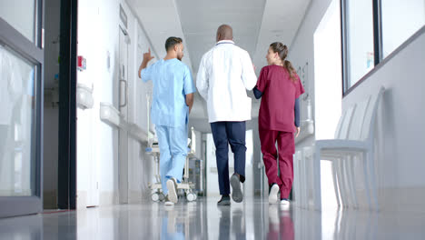 Diverse-male-and-female-doctors-discussing-work-and-walking-in-corridor-at-hospital,-slow-motion