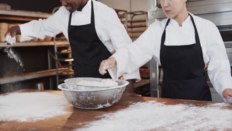 Happy-diverse-bakers-working-in-bakery-kitchen,-pouring-flour-on-counter-in-slow-motion