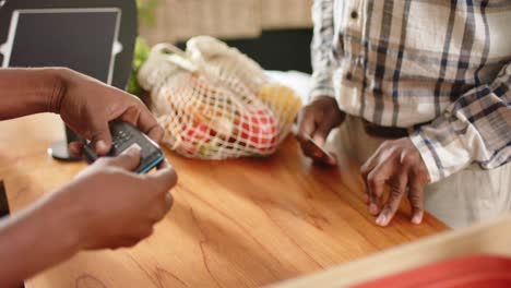 Midsection-of-senior-african-american-man-paying-using-credit-card-at-health-food-shop,-slow-motion