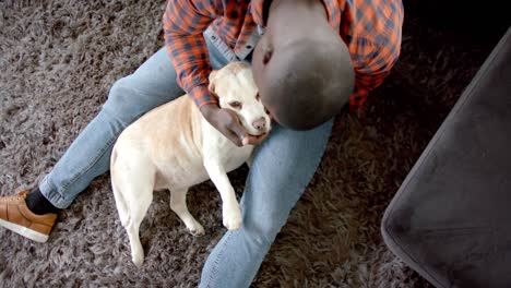 Happy-african-american-man-sitting-on-floor-at-home,-petting-his-pet-dog,-slow-motion