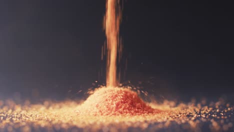 Video-of-close-up-of-orange-sand-grains-pouring-into-heap-and-copy-space-on-black-background
