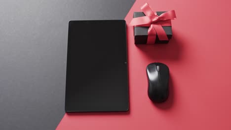 Video-of-tablet-with-blank-screen,-box-and-computer-mouse-on-red-and-black-background
