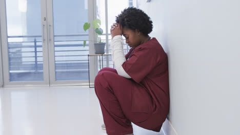 Tired-african-american-female-doctor-squatting-in-hospital-corridor,-slow-motion