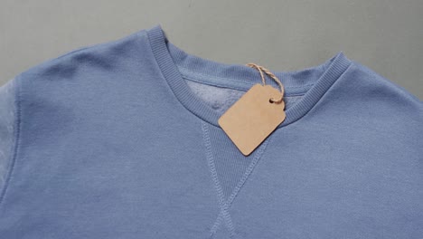 Video-of-flat-lay-of-blue-t-shirt-with-tag-and-copy-space-on-grey-background