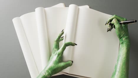 Video-of-halloween-green-monster-hands-and-notebook-with-copy-space-on-grey-background