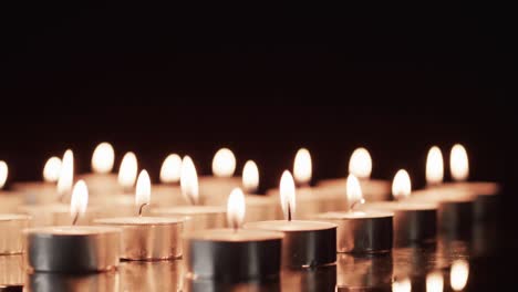 Video-of-rows-of-tea-candles-with-white-flames-and-copy-space-on-black-background