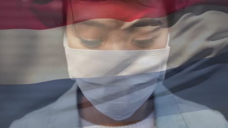 Animation-of-waving-netherlands-flag-against-portrait-of-asian-woman-wearing-face-mask-on-the-street