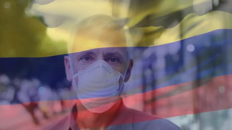 Animation-of-waving-colombia-flag-over-portrait-of-caucasian-man-wearing-face-mask-on-the-street