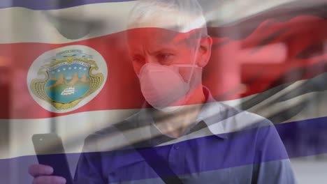 Animation-Des-Schwenkens-Der-Costa-Rica-Flagge-über-Einem-Kaukasischen-Mann-Mit-Gesichtsmaske,-Der-Sein-Smartphone-Auf-Der-Straße-Benutzt