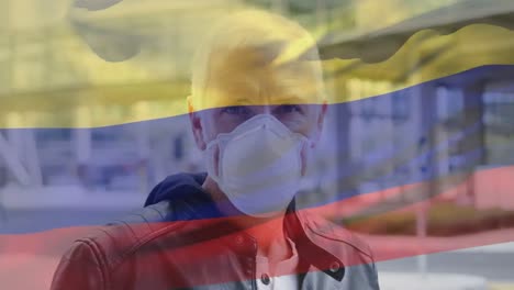 Animation-of-waving-colombia-flag-over-portrait-of-caucasian-man-wearing-face-mask-on-the-street