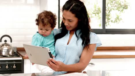 Glückliche-Mutter-Mit-Digitalem-Tablet-Und-Baby-In-Der-Küche