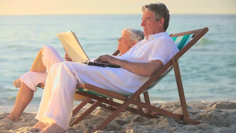 Man-using-a-laptop-on-a-beach-while-his-wife-sleeps-