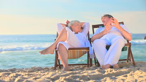 Elderly-couple-sitting-in-deckchairs-on-a-beach