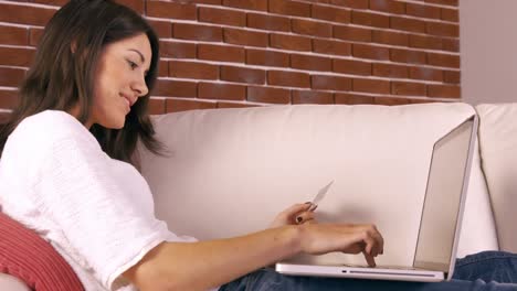 Smiling-woman-with-a-credit-card-and-a-laptop-on-a-sofa