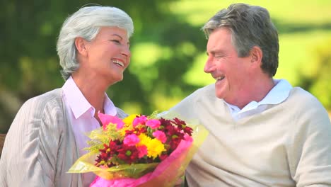 Elderly-couple-holding-a-bunch-of-flowers-while-sitting-on-a-bench