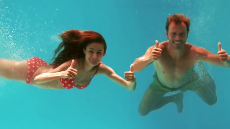 Couple-with-thumbs-up-swimming-underwater