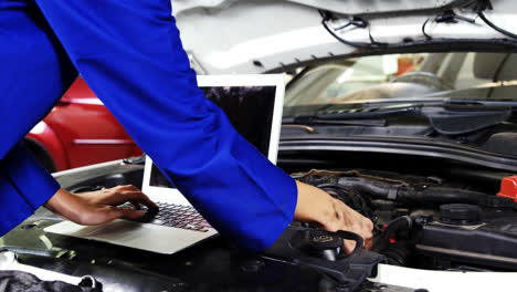Female-mechanic-using-laptop-while-servicing-a-car-engine