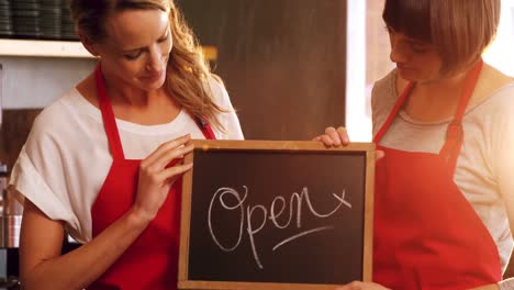 Two-smiling-waitresses-holding-a-open-sign-board