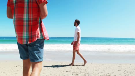 Men-walking-on-beach-while-talking-on-mobile-phone