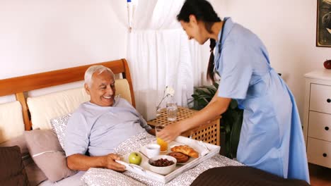 Nurse-serving-breakfast-to-senior-man-in-bedroom