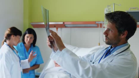 Der-Arzt-Untersucht-Das-Röntgenbild,-Während-Die-Krankenschwester-Im-Hintergrund-Mit-Dem-Patienten-Interagiert
