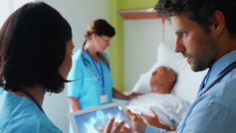 Ärzte-Diskutieren-über-Röntgenaufnahmen-Auf-Einem-Digitalen-Tablet,-Während-Die-Krankenschwester-Im-Hintergrund-Mit-Dem-Patienten-Interagiert