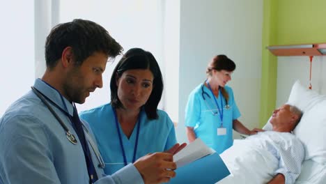 Médicos-Discutiendo-Informes-Mientras-La-Enfermera-Interactúa-Con-El-Paciente-En-Segundo-Plano
