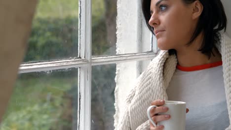 Pensive-woman-sitting-on-windowsill-and-having-cup-of-coffee