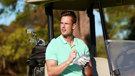 Golfer-sitting-in-golf-buggy-writing-on-paper