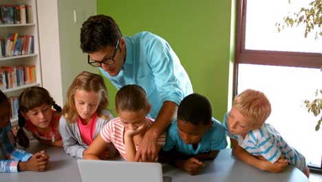 Profesor-Y-Niños-Usando-Una-Computadora-Portátil-En-La-Biblioteca