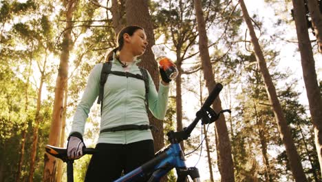 Female-mountain-biker-drinking-water-in-the-forest