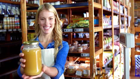 Smiling-female-staff-holding-jar-of-honey-in-supermarket