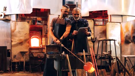 Glassblowers-discussing-over-digital-tablet-while-working-on-a-molten-glass