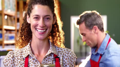 Smiling-female-staff-holding-jar-in-supermarket