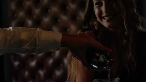 Waiter-pouring-cocktail-in-woman-glass-at-bar-counter
