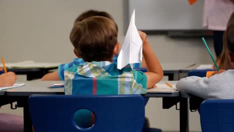 Boy-throwing-paper-plane-while-teacher-teaching-in-classroom