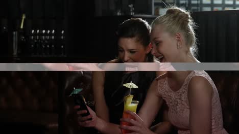 Female-friends-looking-at-mobile-phone-while-having-cocktail
