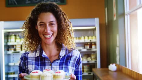 Portrait-of-smiling-woman-holding-plate-of-cup-cake-in-supermarket