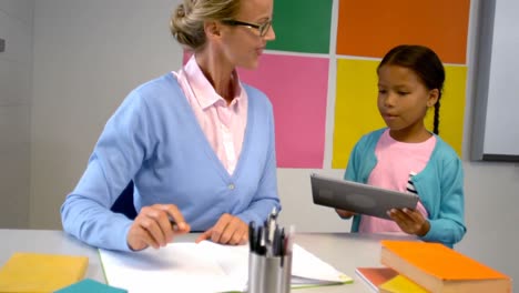 Schoolgirl-and-teacher-using-digital-tablet-in-classroom
