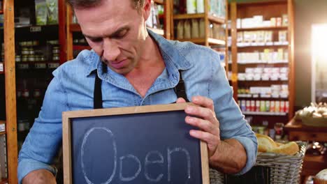 Male-staff-holding-a-open-sign-slate-in-supermarket
