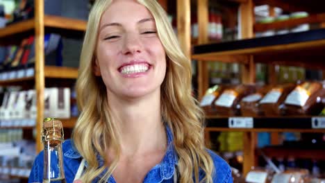 Smiling-female-staff-holding-olive-oil-bottle-in-supermarket