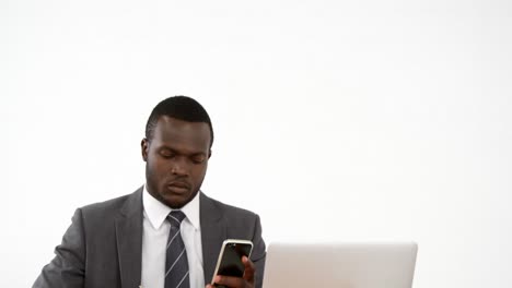 Businessman-writing-in-dairy-while-using-mobile-phone