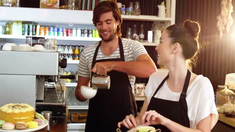 Waitress-wrapping-sandwich-while-waiter-pouring-milk-in-a-cup