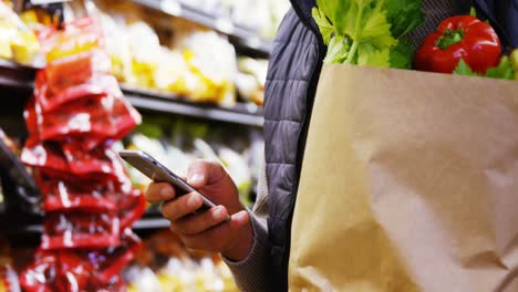 Man-using-mobile-phone-while-holding-grocery-bag