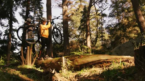 Mountainbike-Paar-Trägt-Fahrrad-Beim-Gehen-Auf-Einem-Baumstamm