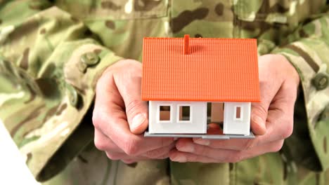 Mid-section-of-soldier-holding-house-model-on-white-background