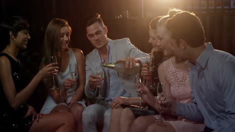 Eine-Gruppe-Lächelnder-Freunde-Sitzt-Auf-Dem-Sofa-Und-Prostet-Ein-Glas-Champagner-An