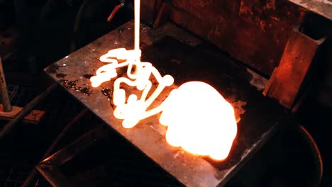 Glassblower-pouring-molten-glass-on-metal-work-bench