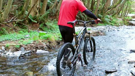 Mountain-biker-walking-with-bicycle-in-creek